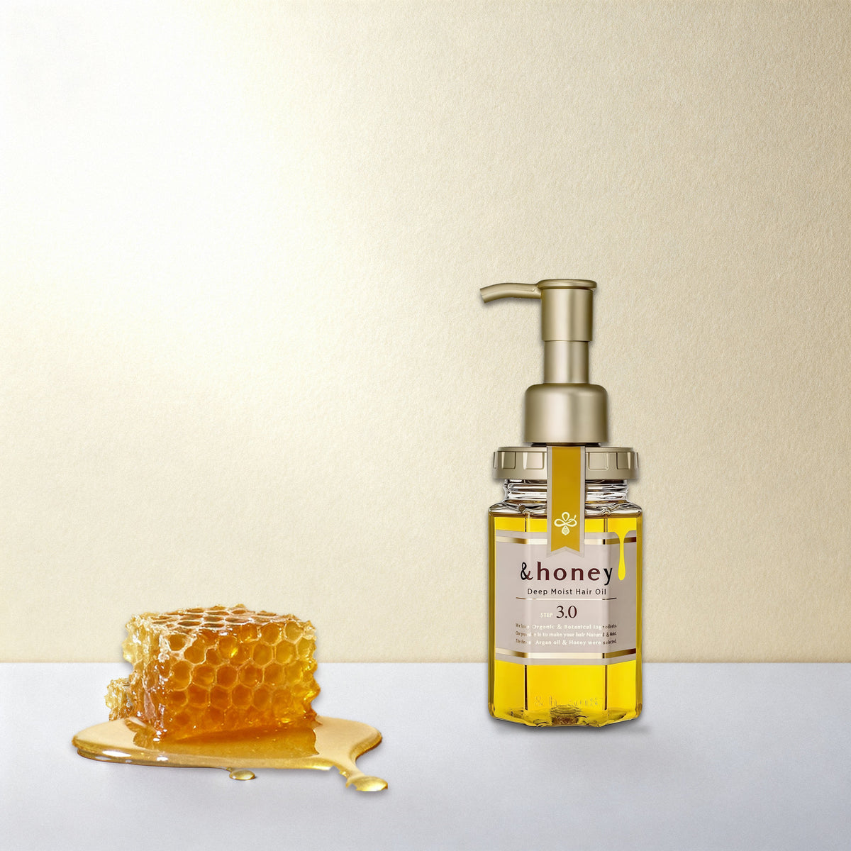 שמן השיער honey& 3.0 על משטח בהיר, לצד חלת דבש
